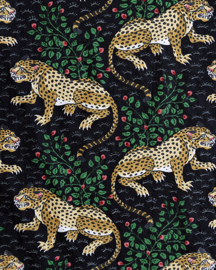 Close-up of the Bagheera print with spotted leopards, leafy branches, and red flowers on a black background