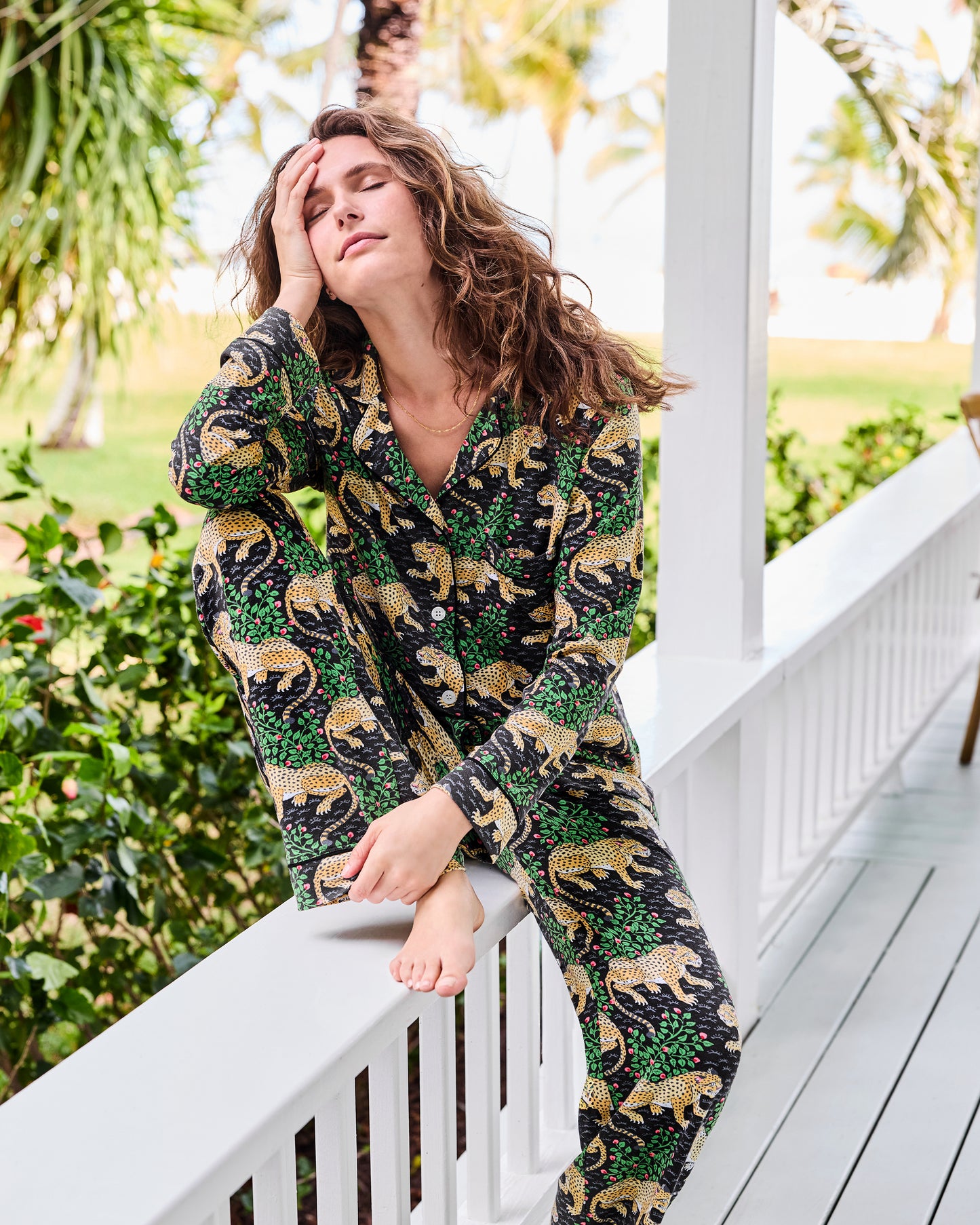 Person sitting on a porch railing wearing a black long-sleeve leopard-and-floral print pajama set.