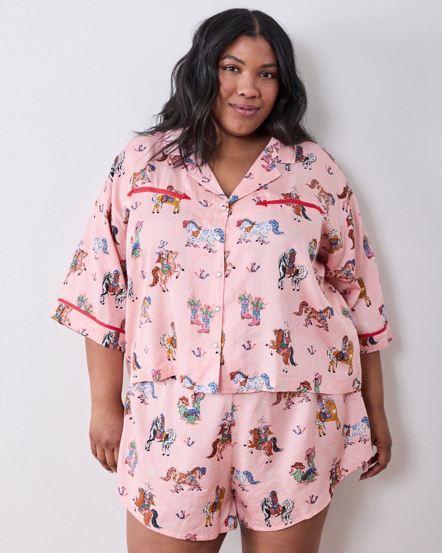 Model wearing the pink short pajama set with a horse-and-cowgirl print, collared button-front top, and matching shorts.