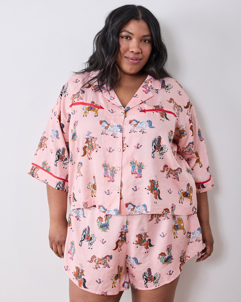 Model wearing the pink short pajama set with a horse-and-cowgirl print, collared button-front top, and matching shorts.