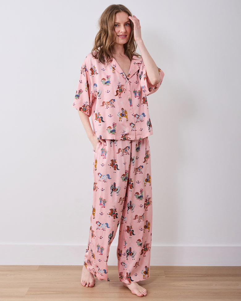 Full-length model wearing the pink long pajama set with a horse-and-cowgirl print, short-sleeved collared top, and wide-leg pants.