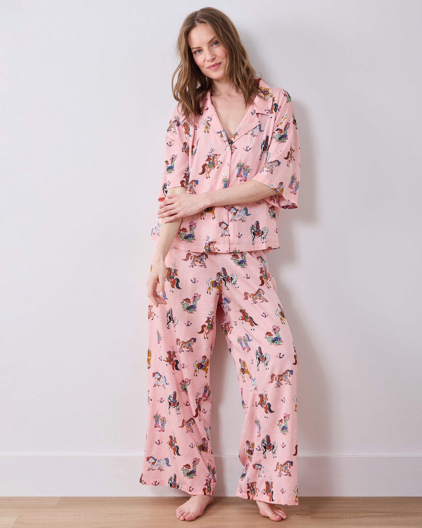 Full-length view of a pink cowgirl-print pajama set with a short-sleeved button-down top and wide-leg pants.