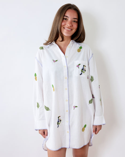 Front view of a white oversized button-down sleep shirt with full-length sleeves and pineapple, leaf, flower, and toucan embroidery.