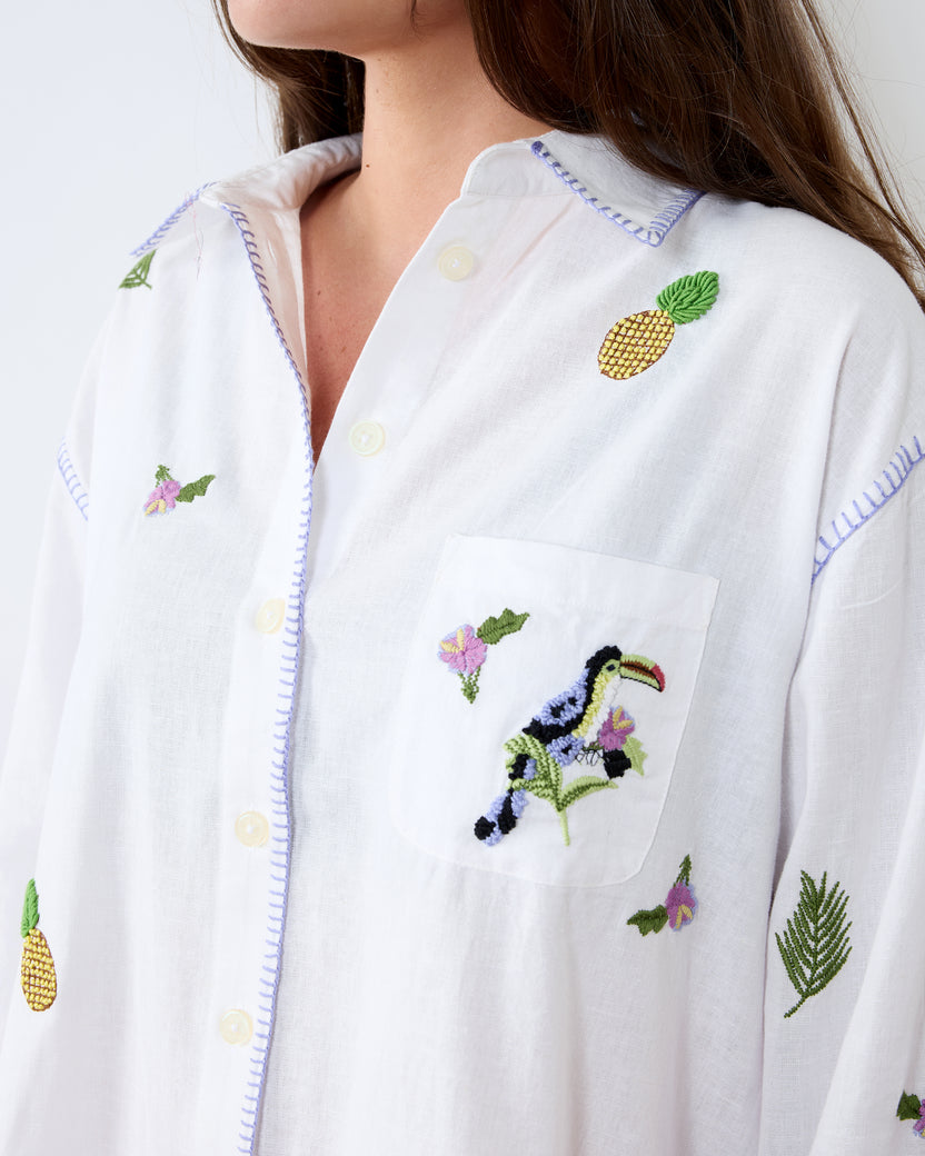 Close-up of the white button-down shirt showing the collar, front buttons, pocket, and toucan and floral embroidery.