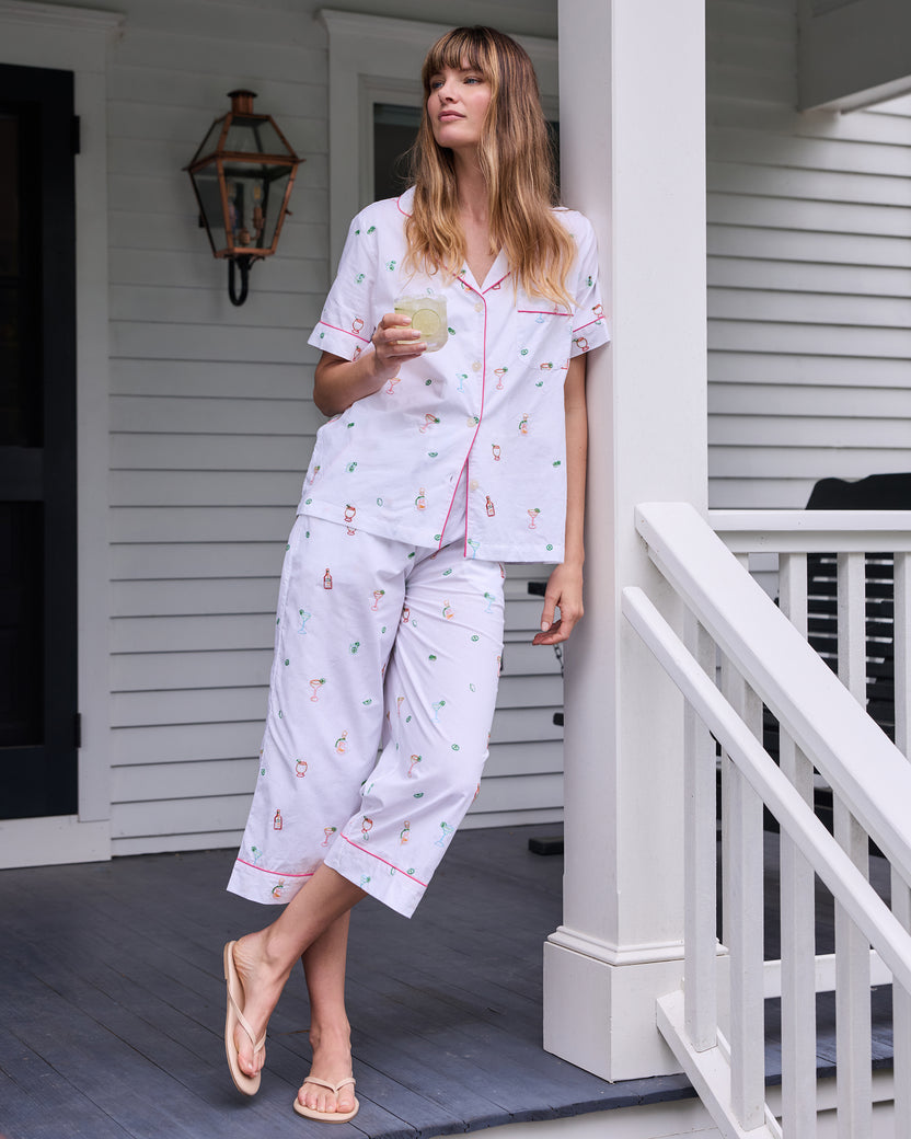 Person wearing the cloud short-sleeve pajama top and cropped pants with embroidered cocktail-themed motifs while holding a glass on a porch.