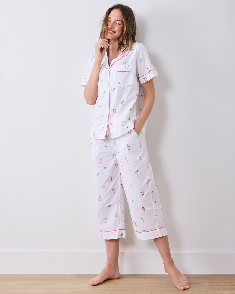 Full-length front view of a person wearing the cloud short-sleeve pajama top and cropped pants with pink piping and embroidered cocktail-themed motifs.
