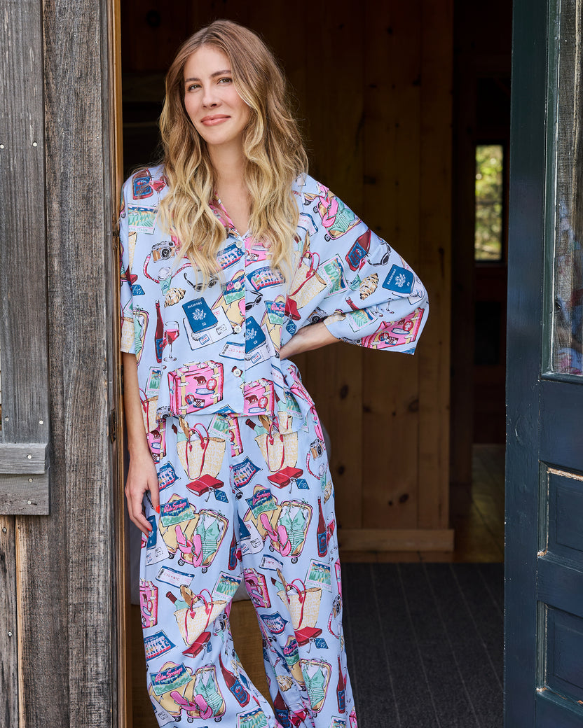 Person wearing a pale blue short-sleeve button-front pajama set with a travel-themed print, standing in a doorway.