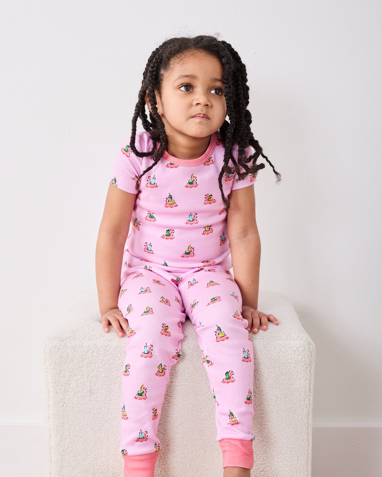 Child seated in the pink Flamingo Floaties short-sleeve pajama top and pants, shown from the front