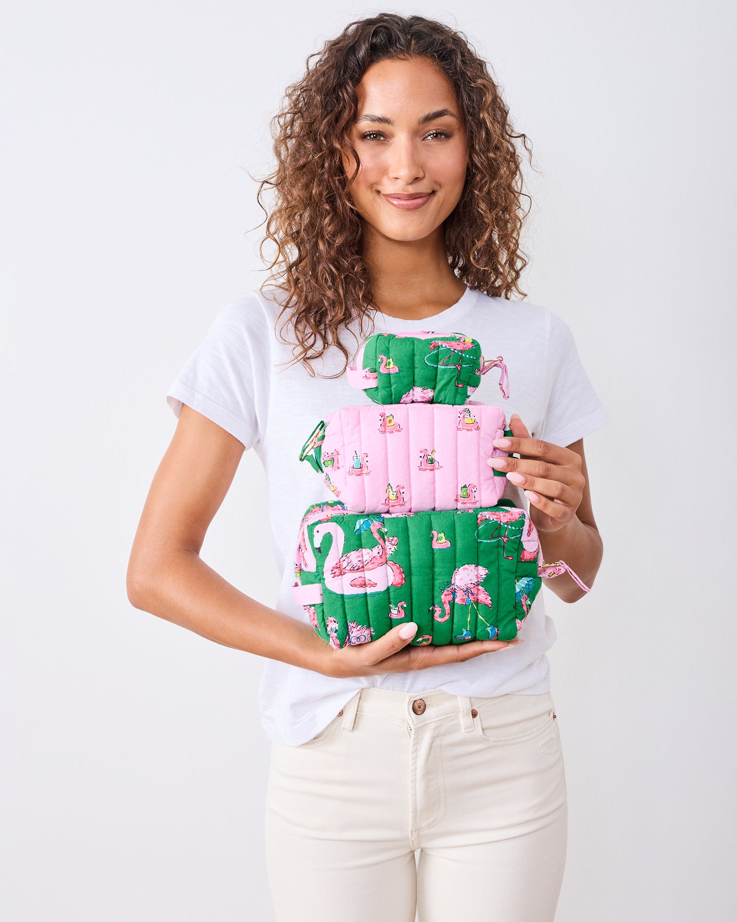 Model holding three quilted flamingo-print pouches stacked from large to small