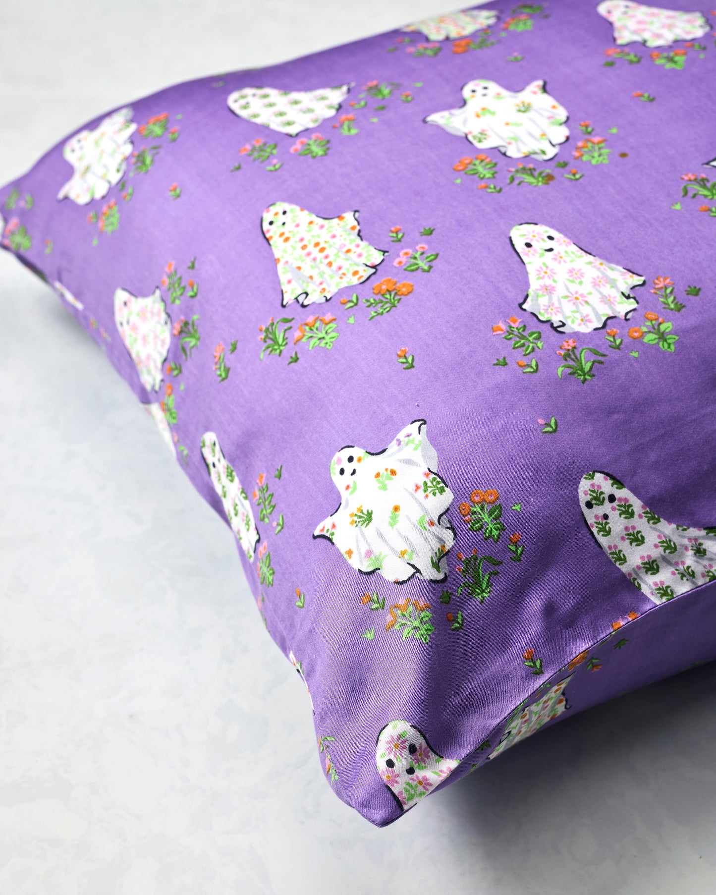 Purple Gardening Ghosts pillowcase spread out to show its repeating white ghost and floral print.