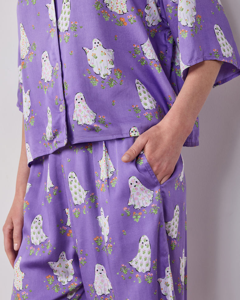 Close-up of a purple pajama set with white ghost and floral prints, showing the top hem and a pants pocket.