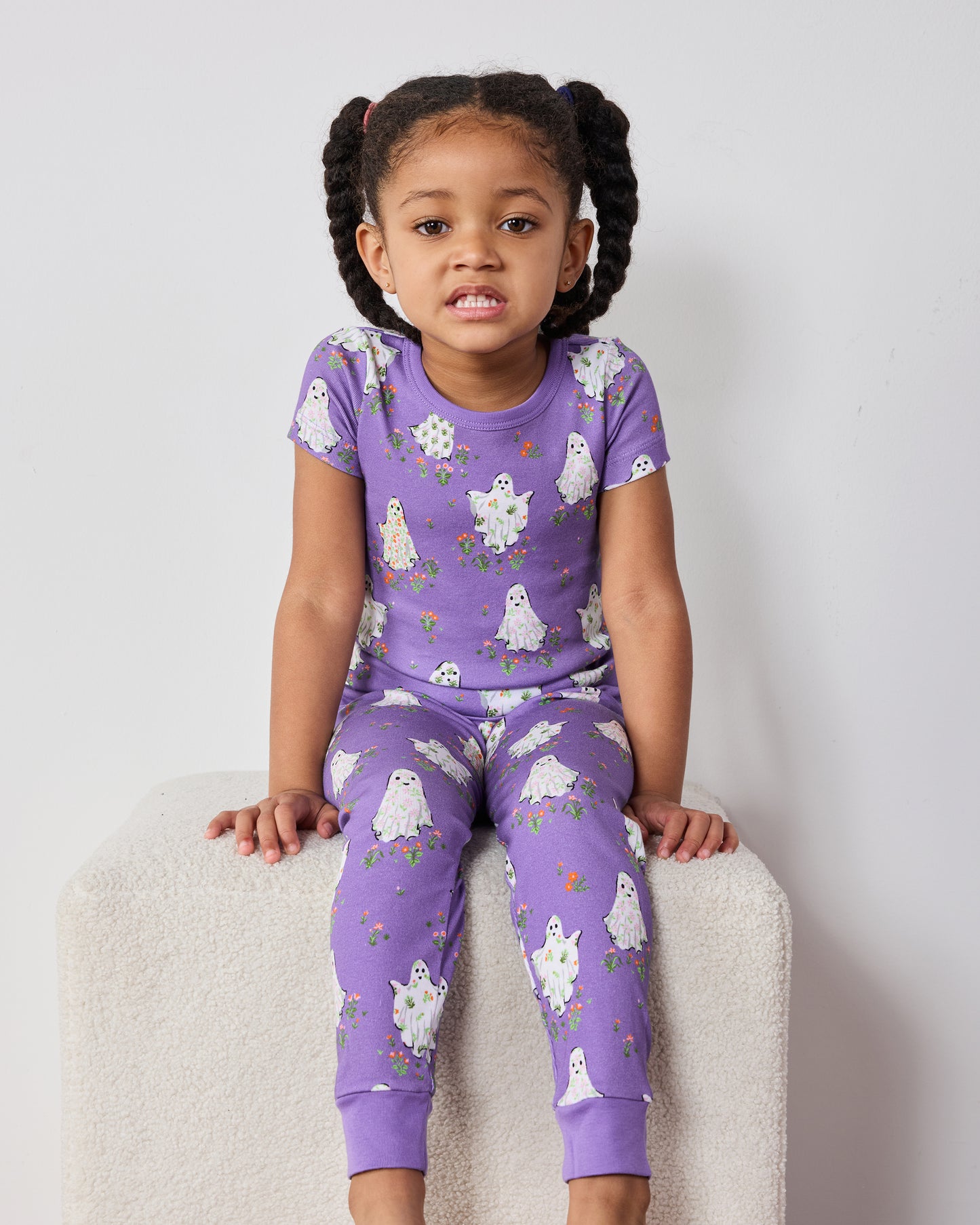 Child seated wearing a purple short-sleeve ghost-print pajama top and matching pants