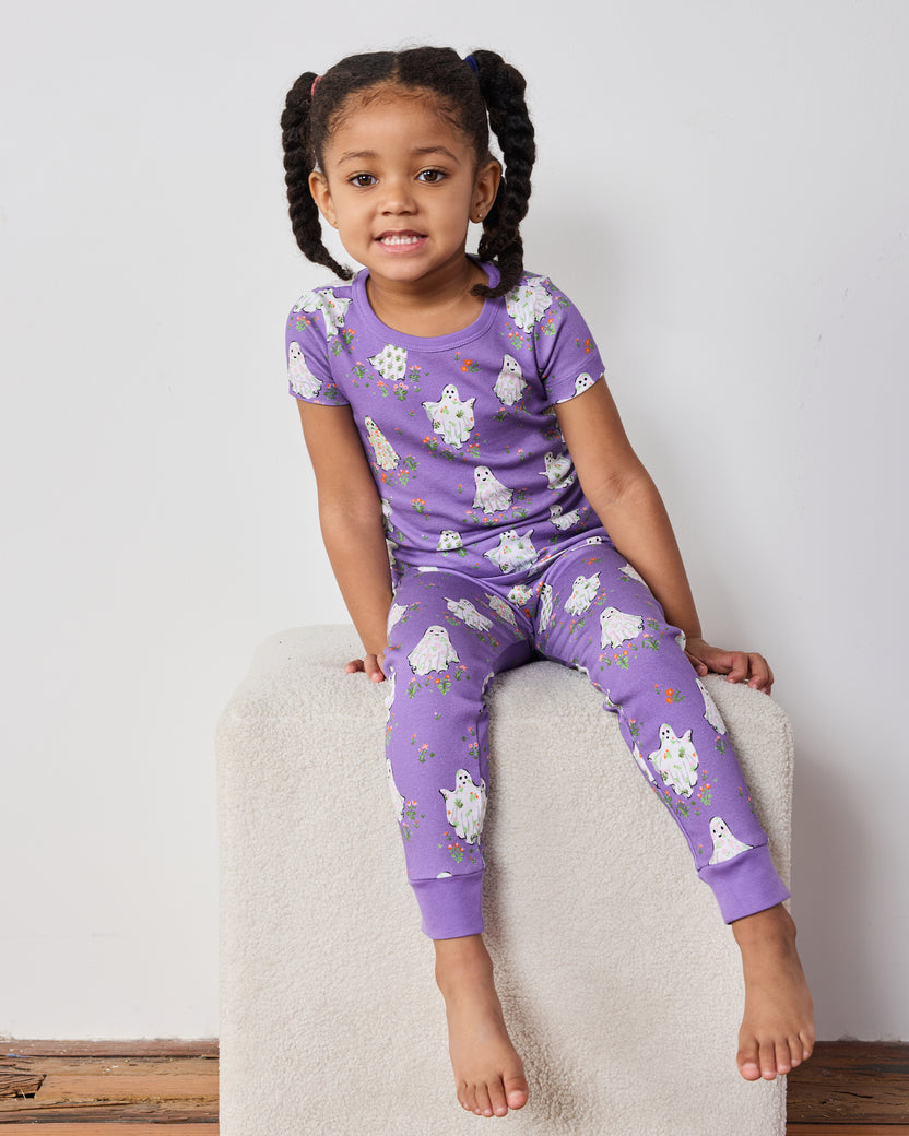 Child seated on a block wearing a purple short-sleeve ghost-print pajama set