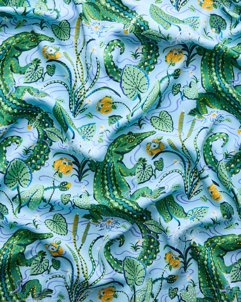 Close-up of the blue-green print with gators, leaves, flowers, and winding water lines