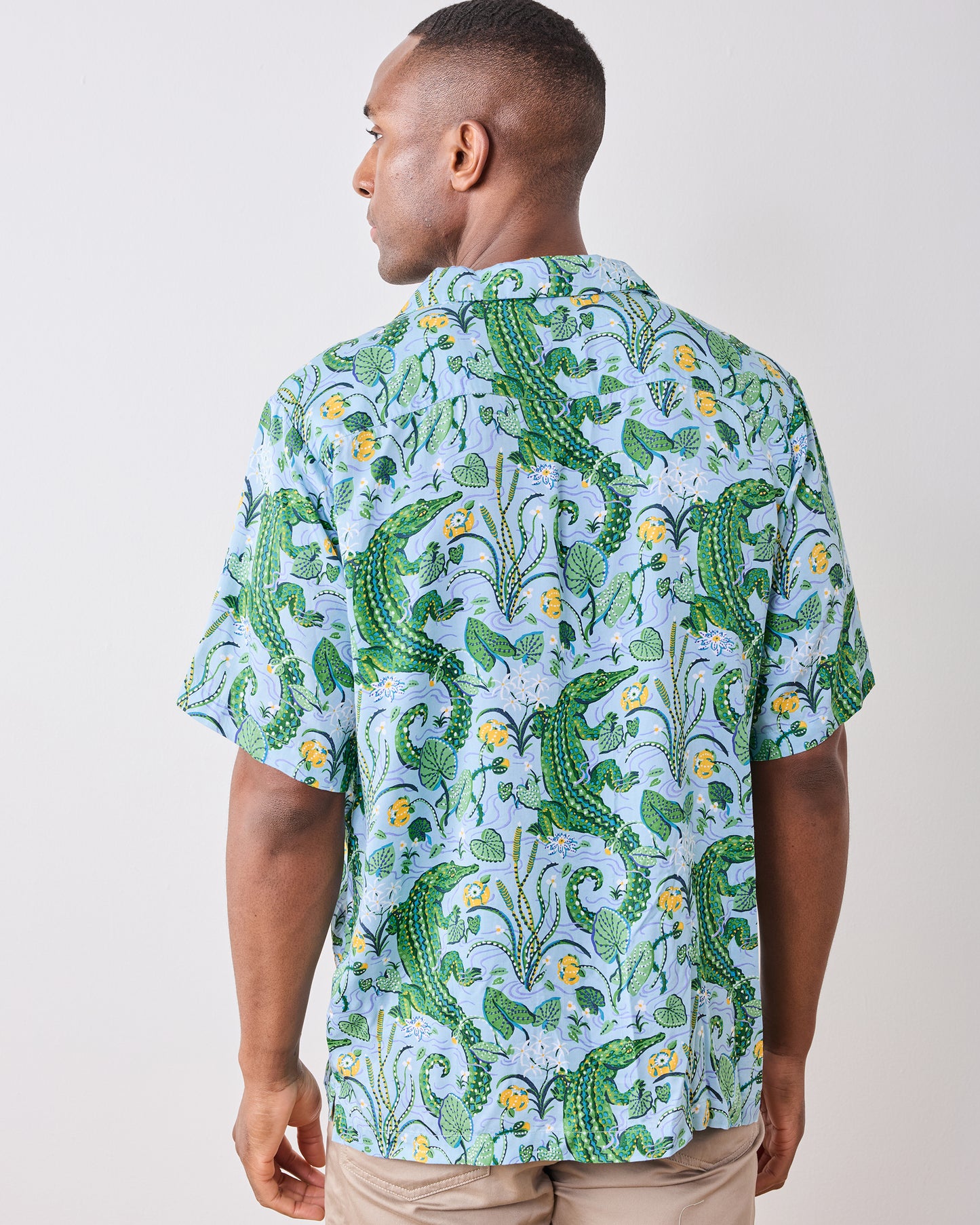 Back view of a model wearing the Blue Lagoon camp shirt with an alligator and foliage print