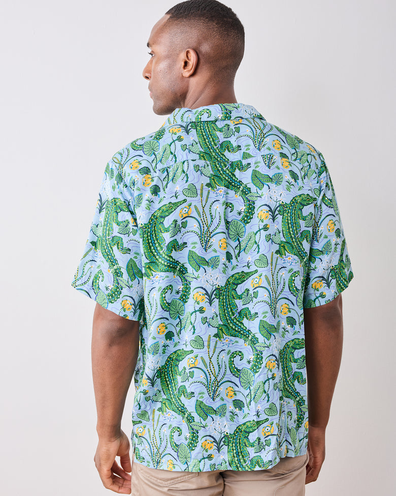 Back view of a model wearing the Blue Lagoon camp shirt with an alligator and foliage print
