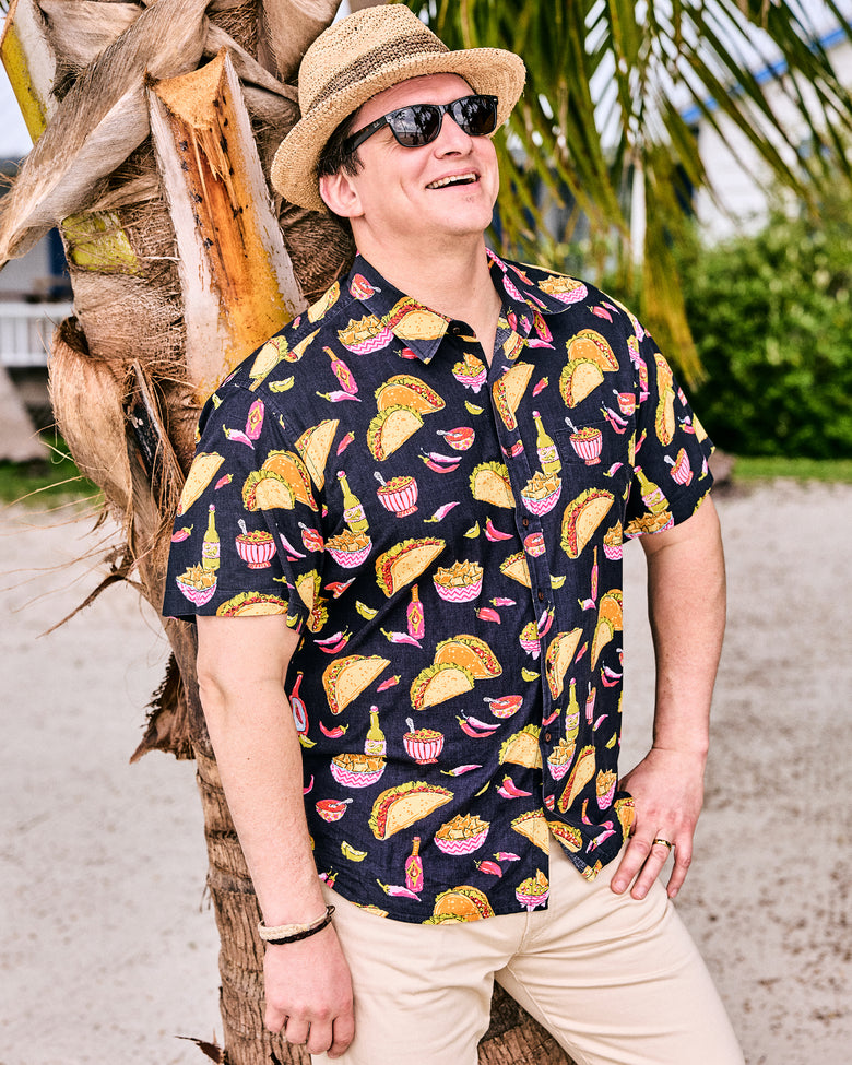 Model wearing the short-sleeve Guac On button-down shirt with beige trousers, sunglasses, and a straw hat