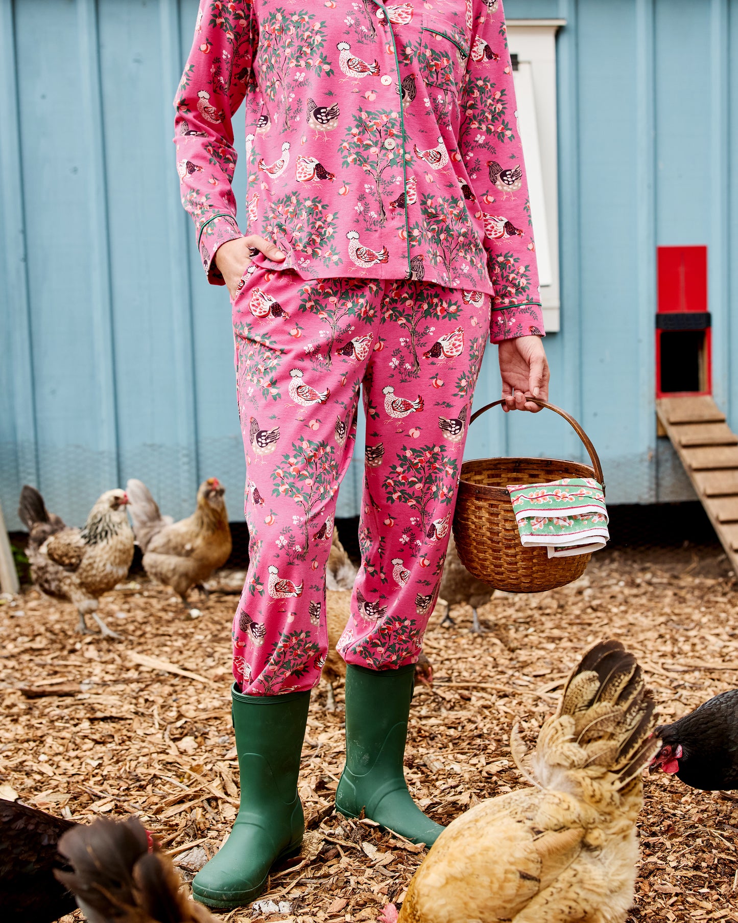 Close view of the pink Hen House long pajama set with a button-front top, long pants, and chicken-and-floral print, worn with green boots.