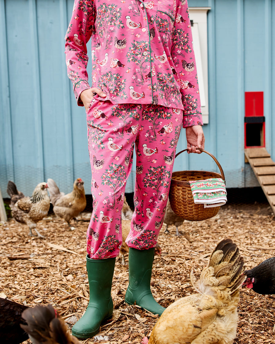 Close view of the pink Hen House long pajama set with a button-front top, long pants, and chicken-and-floral print, worn with green boots.
