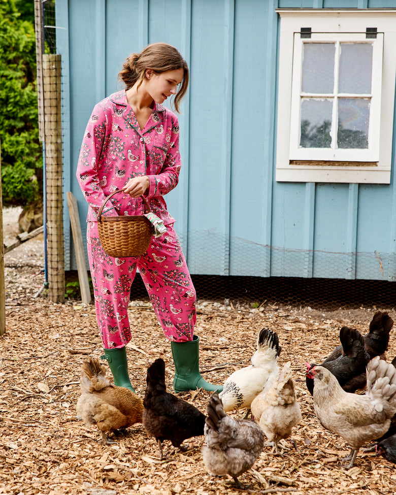 Model wearing the pink Hen House long pajama set and holding a basket among chickens outside a blue coop.
