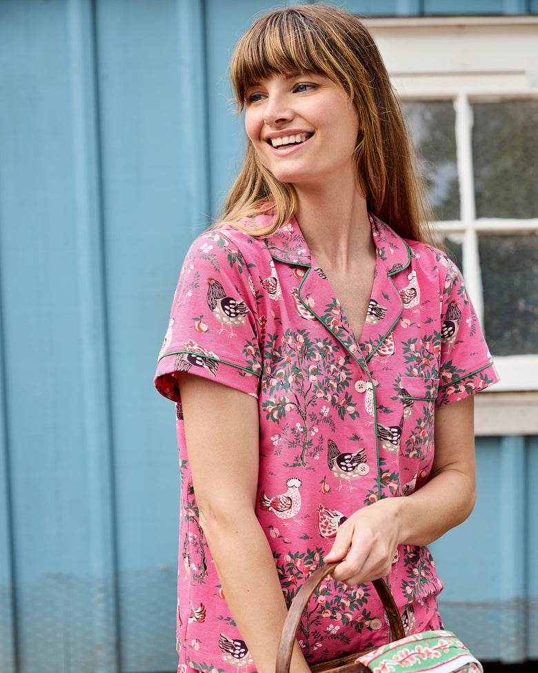 Model wearing the pink Hen House short pajama set with a button-front top, shorts, and chicken-and-floral print.