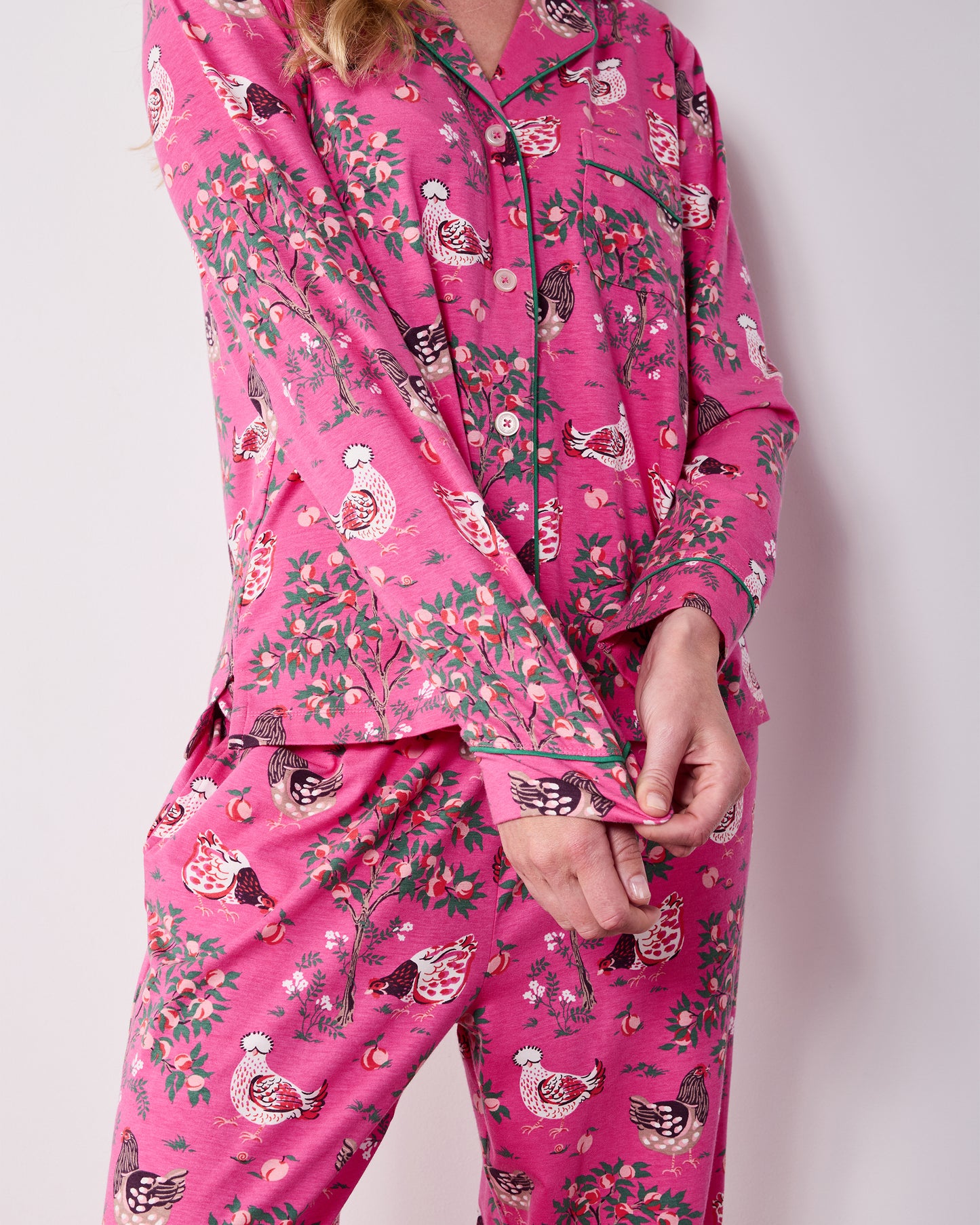 Close front view of the Rose Pop Hen House pajama top and matching pants, showing the button front, green piping, chest pocket, and chicken-and-floral print.