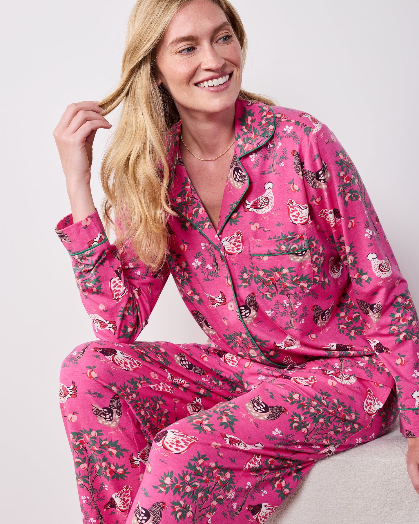 Front view of the Rose Pop Hen House long pajama set worn while seated, showing the button-down top, chest pocket, and matching chicken-and-floral print pants.