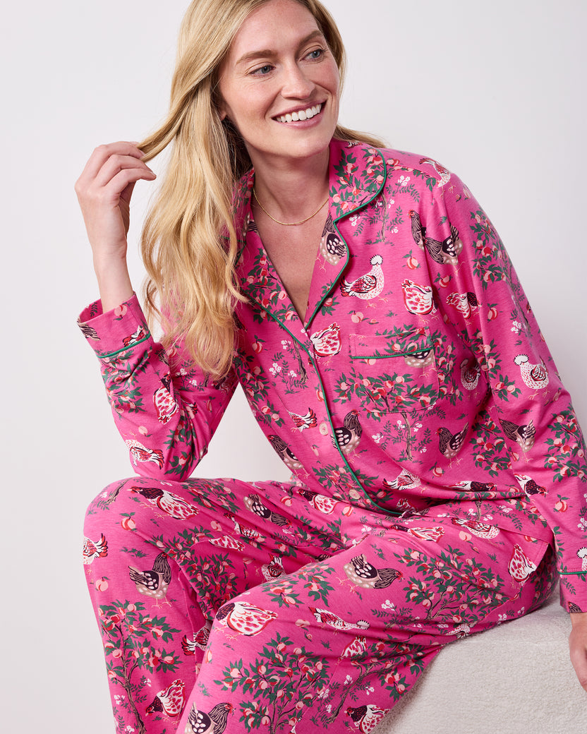 Front view of the Rose Pop Hen House long pajama set worn while seated, showing the button-down top, chest pocket, and matching chicken-and-floral print pants.