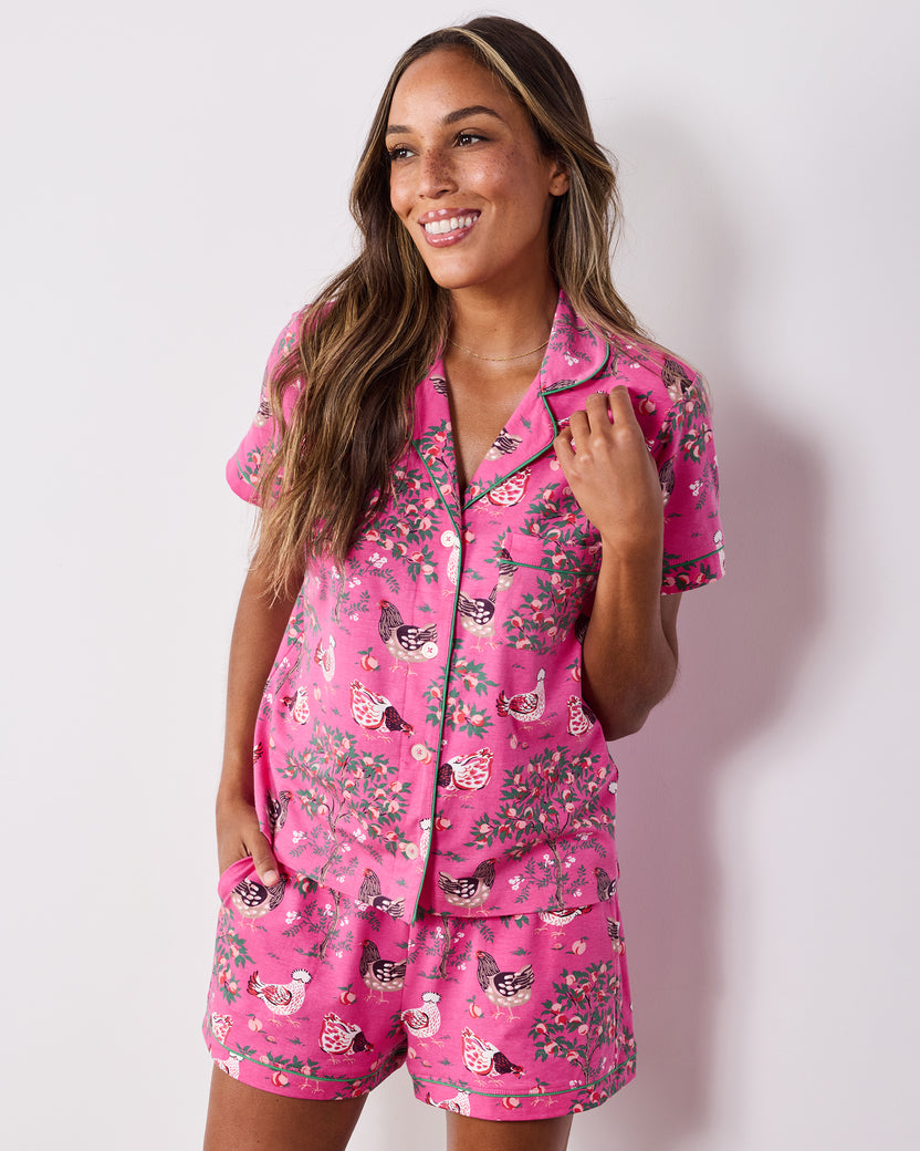 Three-quarter view of the Rose Pop Hen House short pajama set with a collared button-down top, matching pocketed shorts, and chicken-and-floral print.
