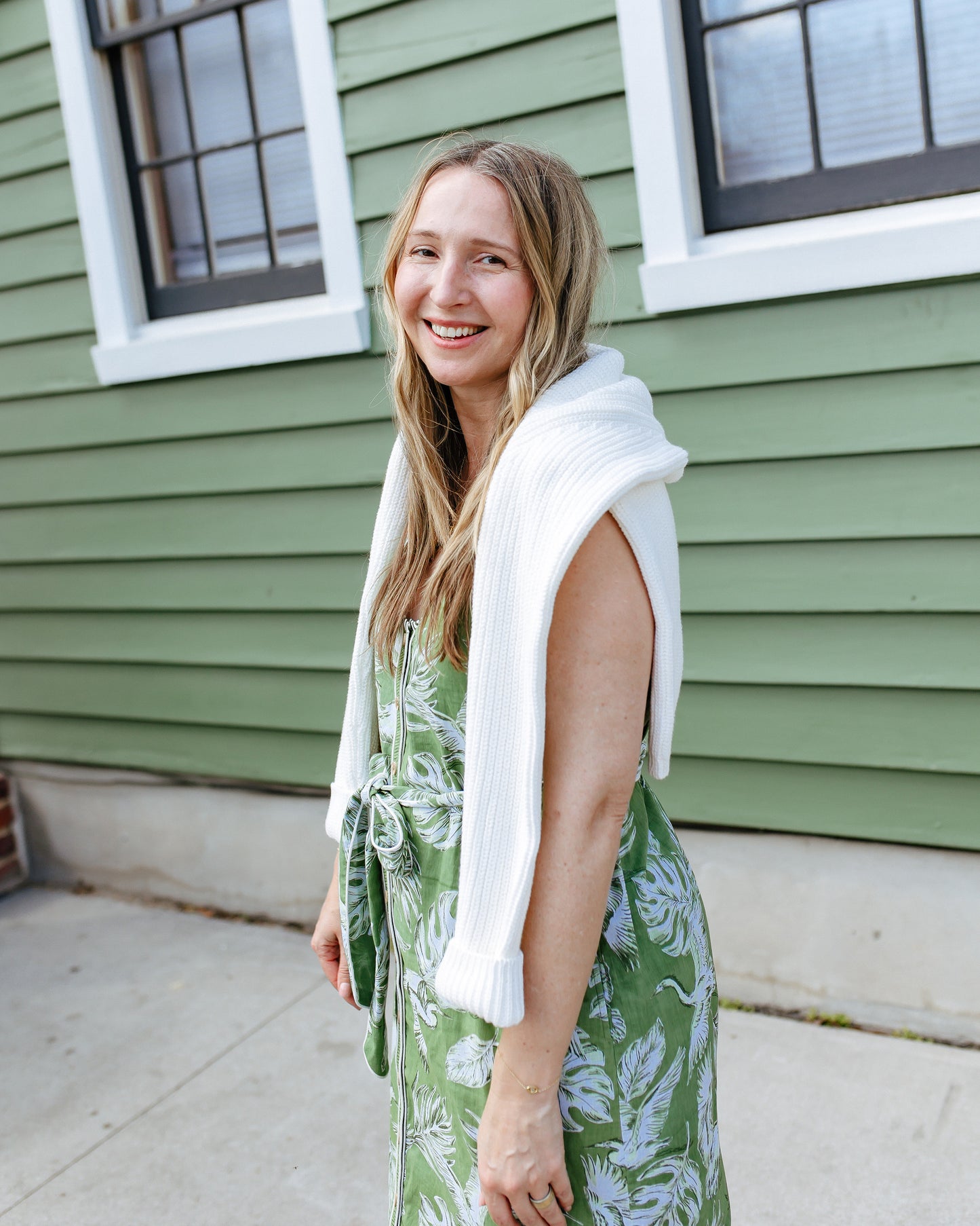 Side view of the Heron Landing Alma Dress with the waist belt tied in a bow and a white sweater draped over the shoulders