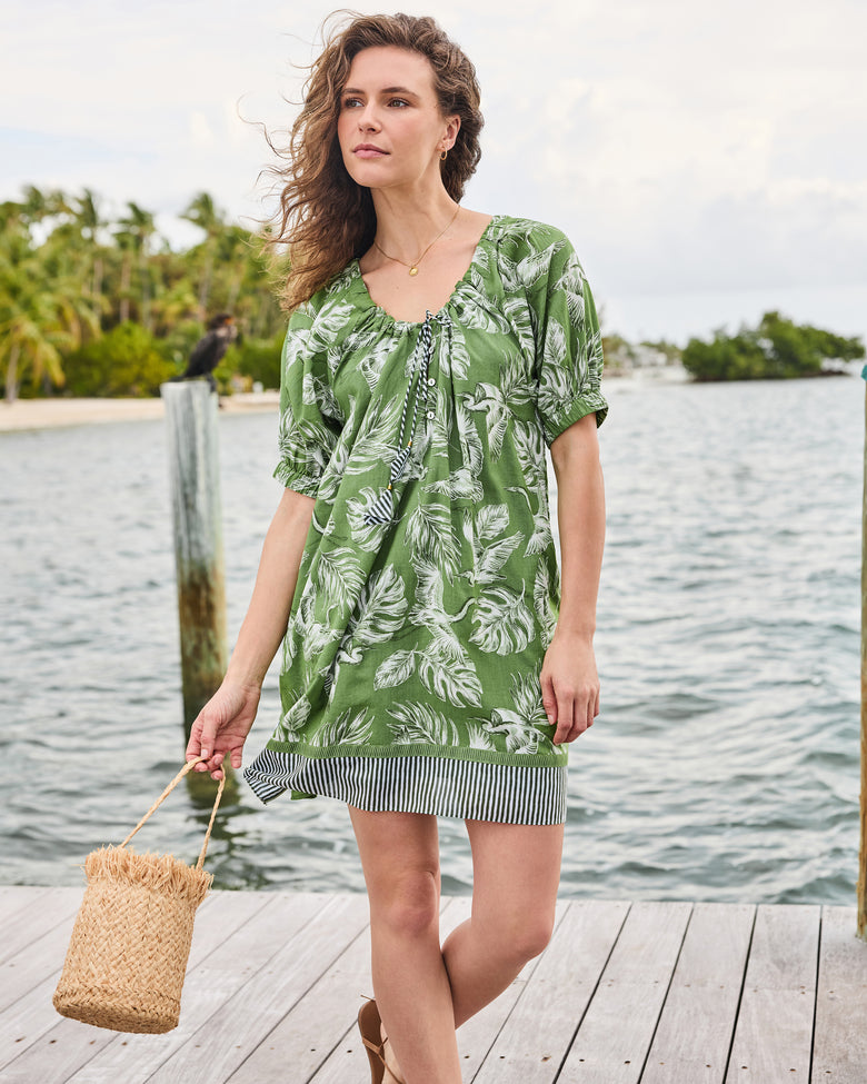 Full front view of the olive grove Annie Dress with gathered tie neckline and striped hem, styled with a woven bag