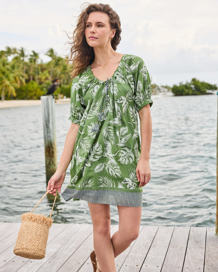 Full front view of the olive grove Annie Dress with gathered tie neckline and striped hem, styled with a woven bag