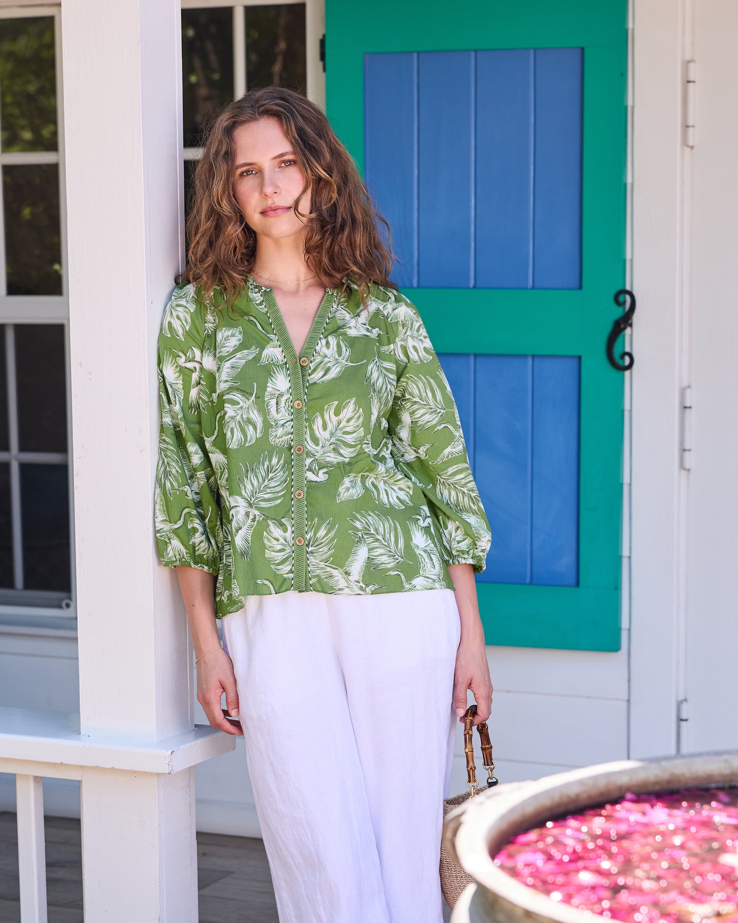 Model wearing the olive-green Frankie Blouse with white bird and tropical leaf print, shown from the front with white trousers