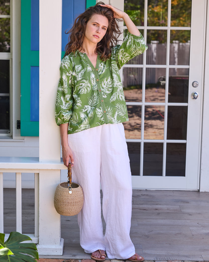 Full-length front view of the olive-green Frankie Blouse with white bird and tropical leaf print, paired with white trousers