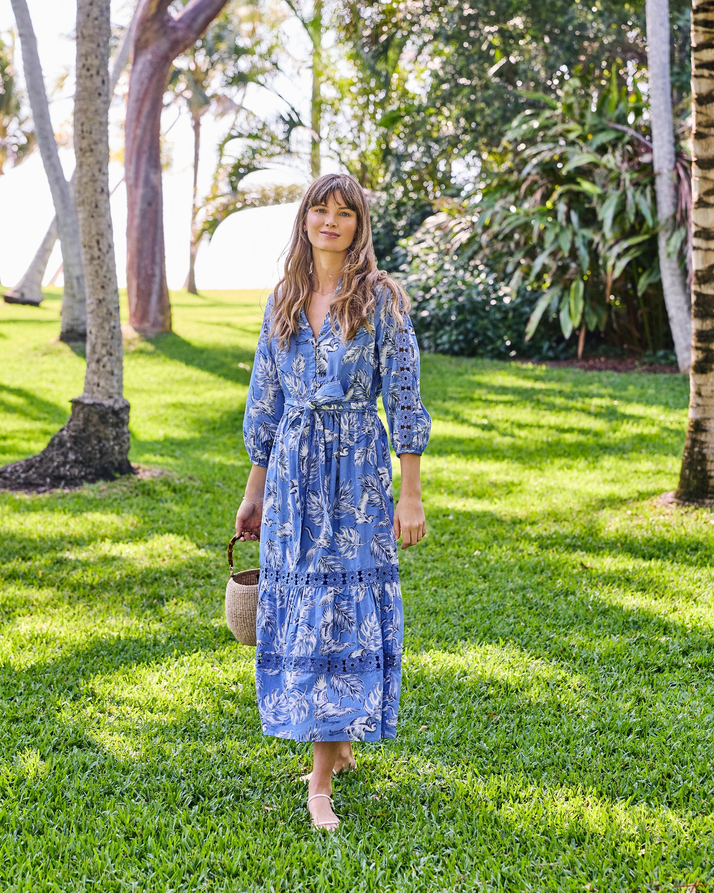 Full-length front view of the saltwater blue Monroe dress with a heron-and-leaf print, tie belt, and lace panels