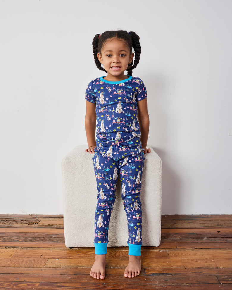 Child standing and wearing a blue short-sleeve top and matching pants with a colorful laboratory-themed print.