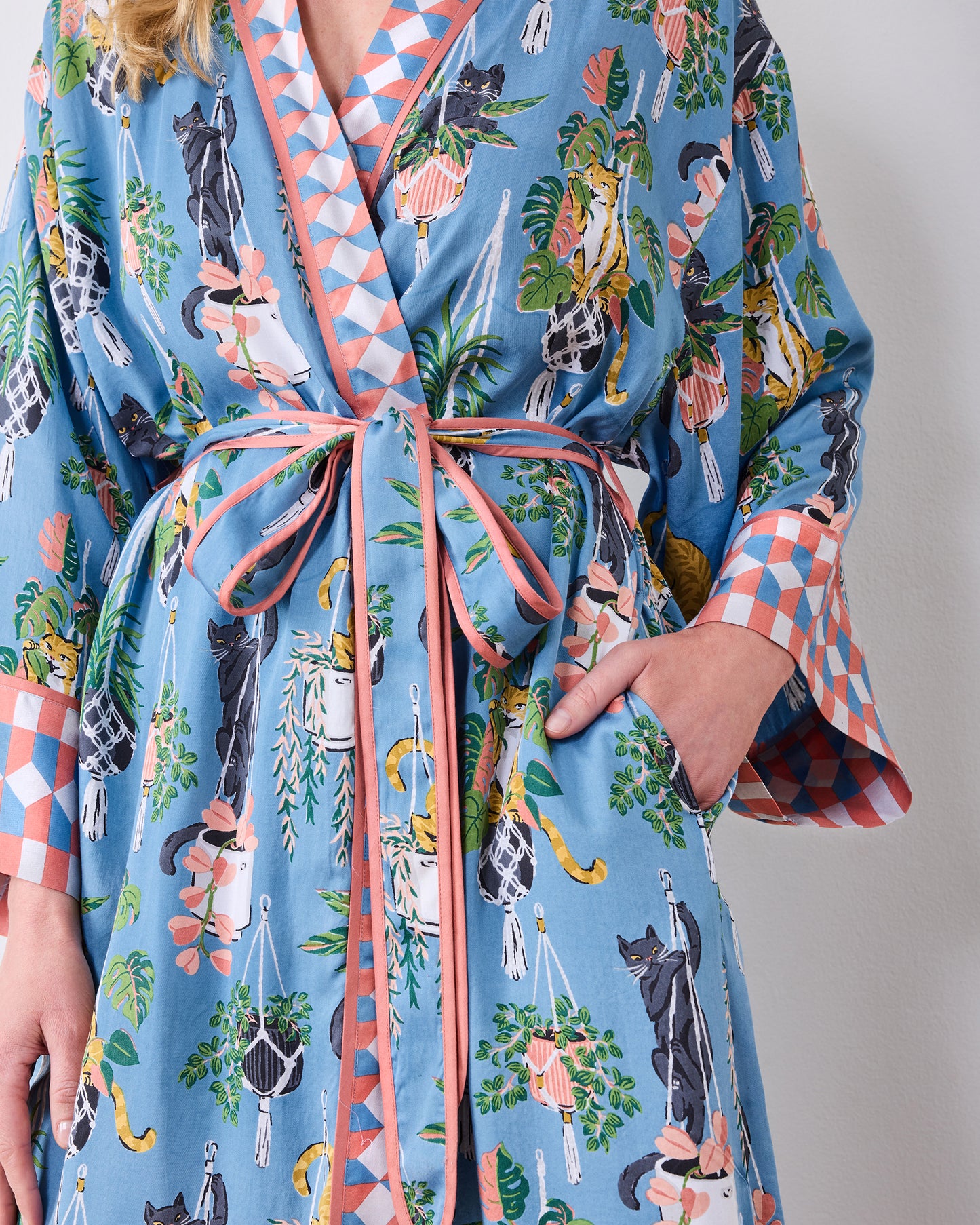 Close-up of the robe's tied belt, pocket, cat-and-houseplant print, and patterned cuffs