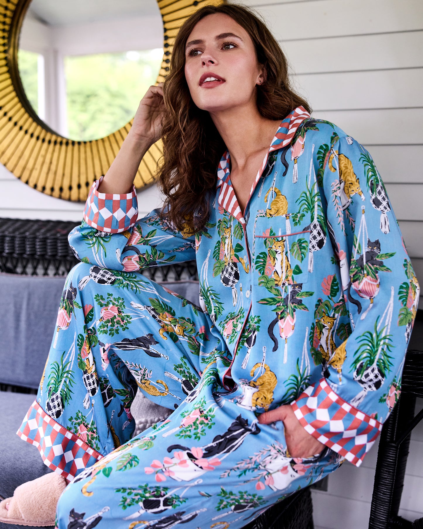 Person seated indoors wearing a blue pajama set with cat, houseplant, and geometric cuff prints.
