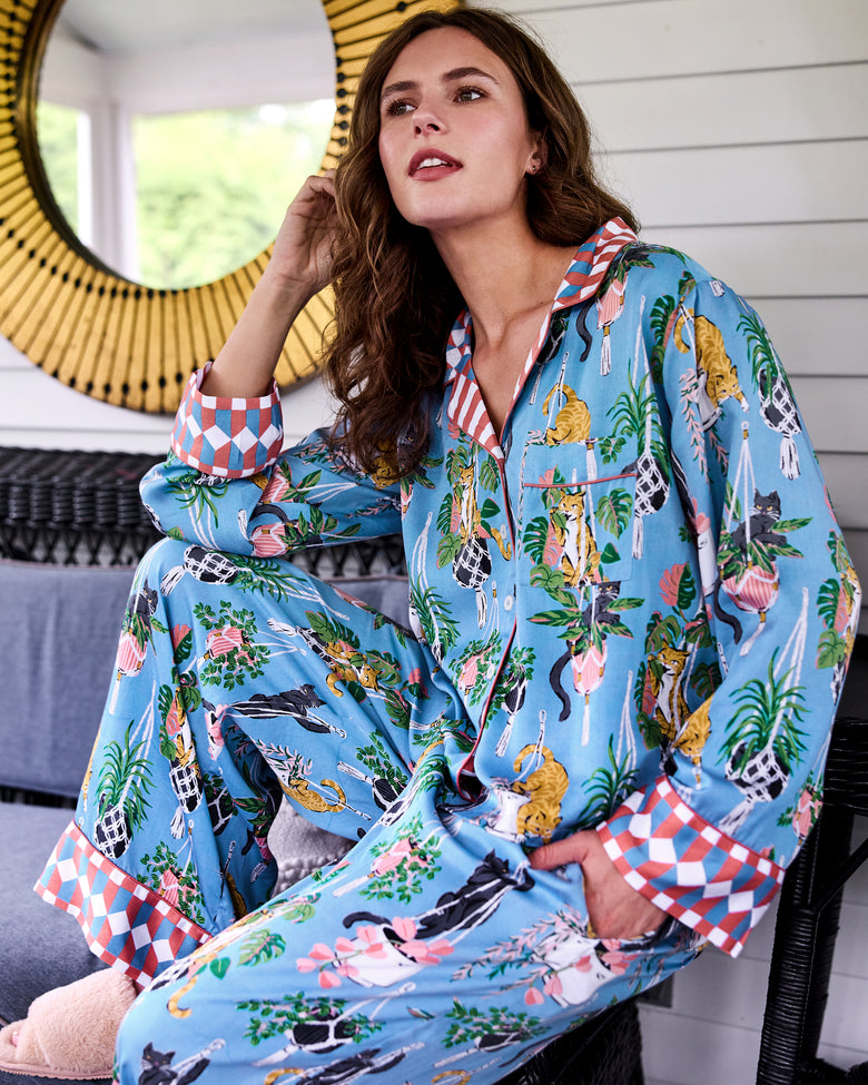 Person seated indoors wearing a blue pajama set with cat, houseplant, and geometric cuff prints.