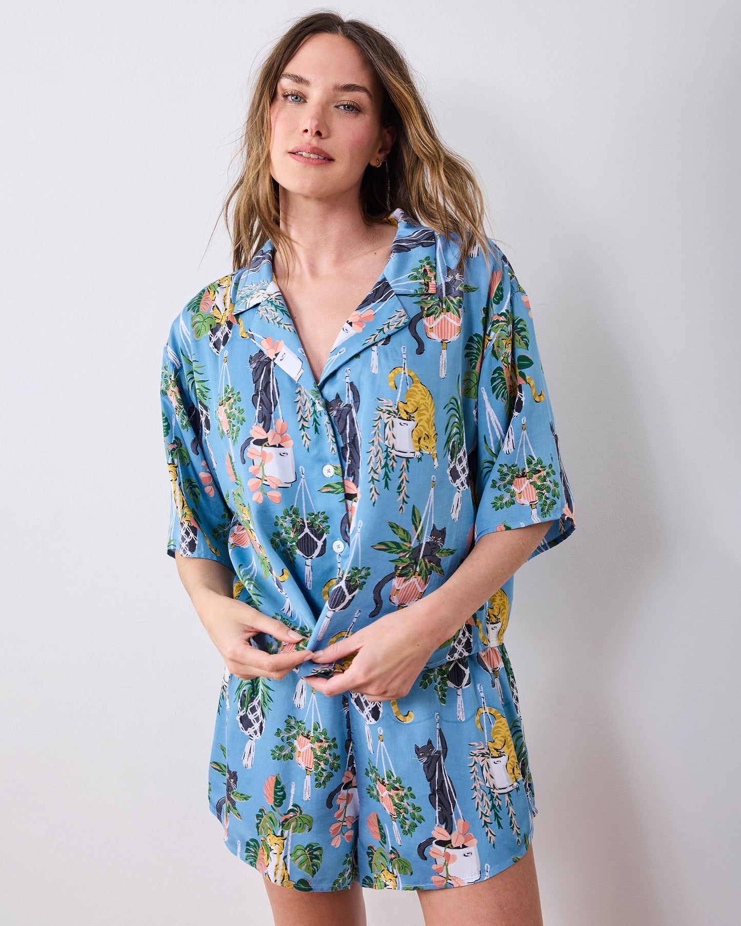Front three-quarter view of the slate blue short pajama set with cats and hanging plants print