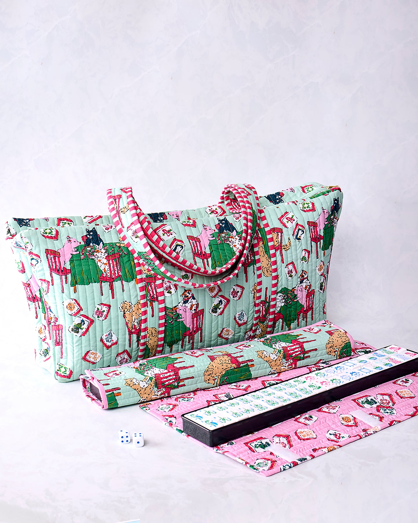Pale jade quilted Mah Jongg bag with handles and a playful printed scene, shown with a rolled item, game rack, mat, and tiles.