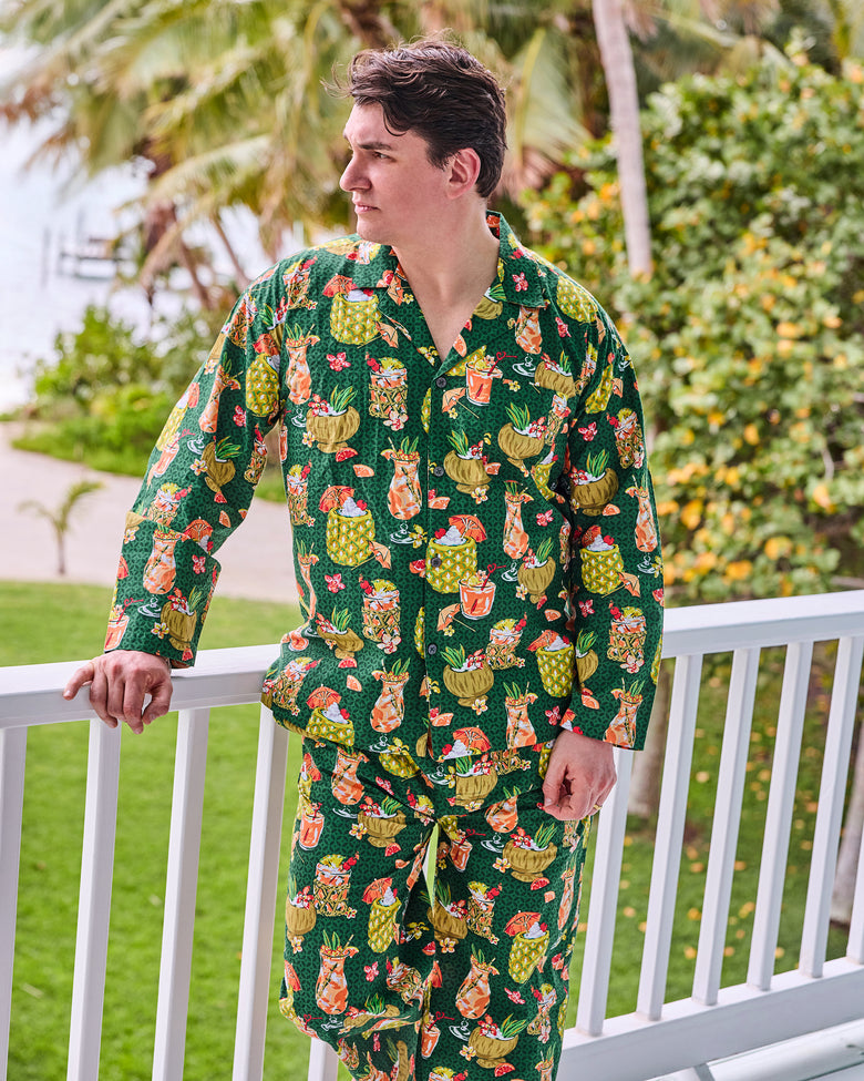 Model wearing the green tropical drink-print long pajama set beside a porch railing
