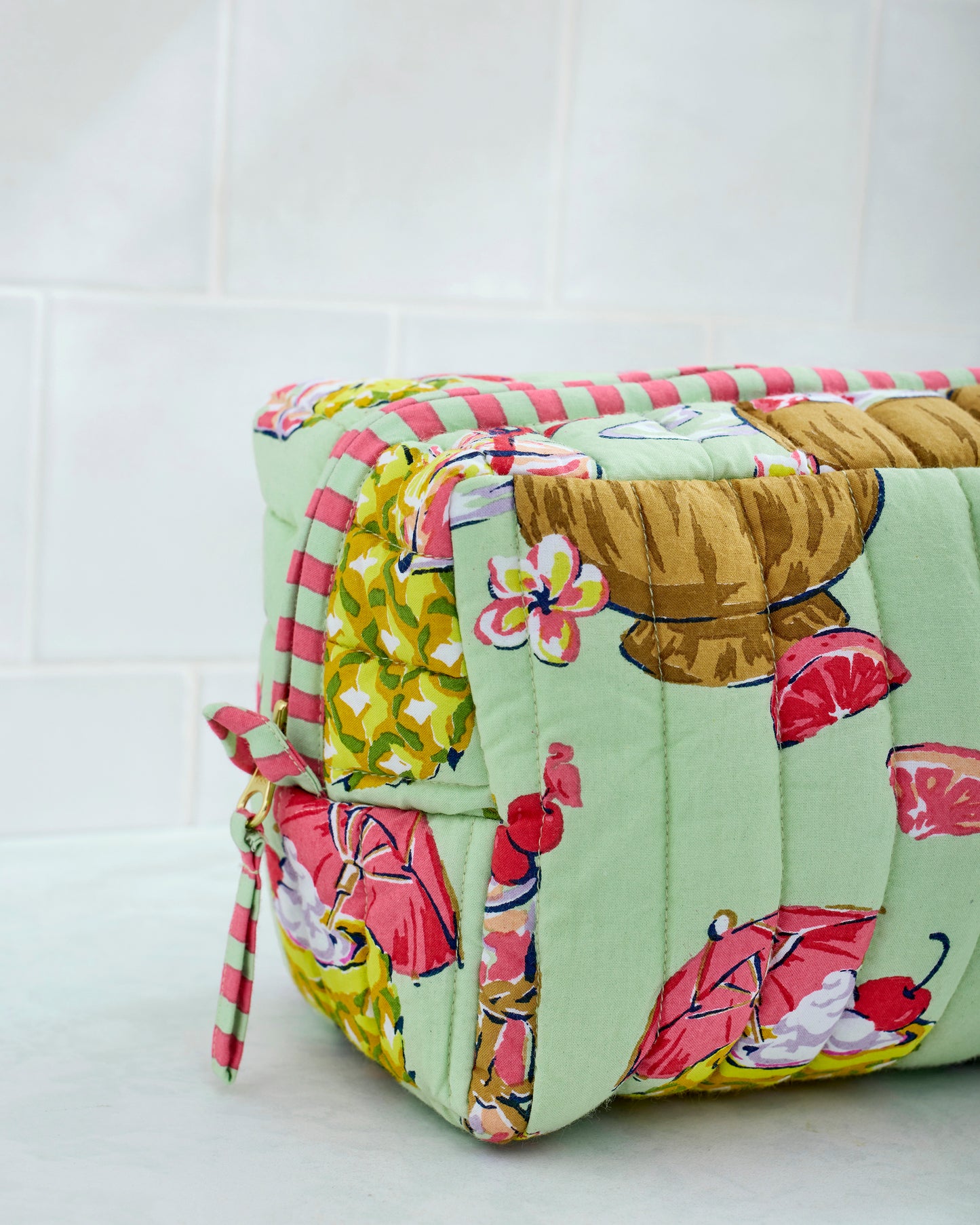 Angled close-up of the Mojito quilted pouch showing its striped trim, zipper, and tropical drink print