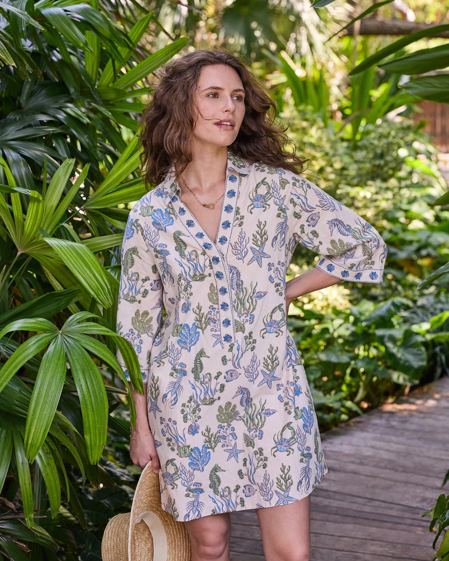 Three-quarter front view of the knee-length Goa Dress with wide sleeves and blue-and-green sea-life print on a sand-colored background