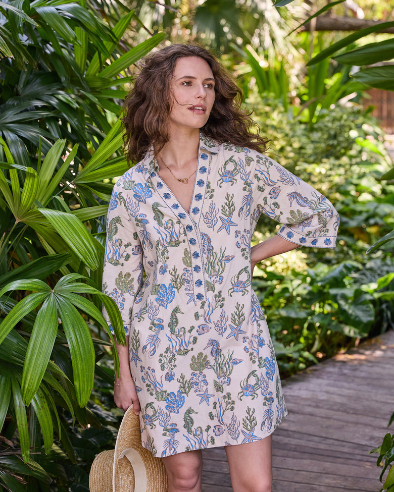 Three-quarter front view of the knee-length Goa Dress with wide sleeves and blue-and-green sea-life print on a sand-colored background