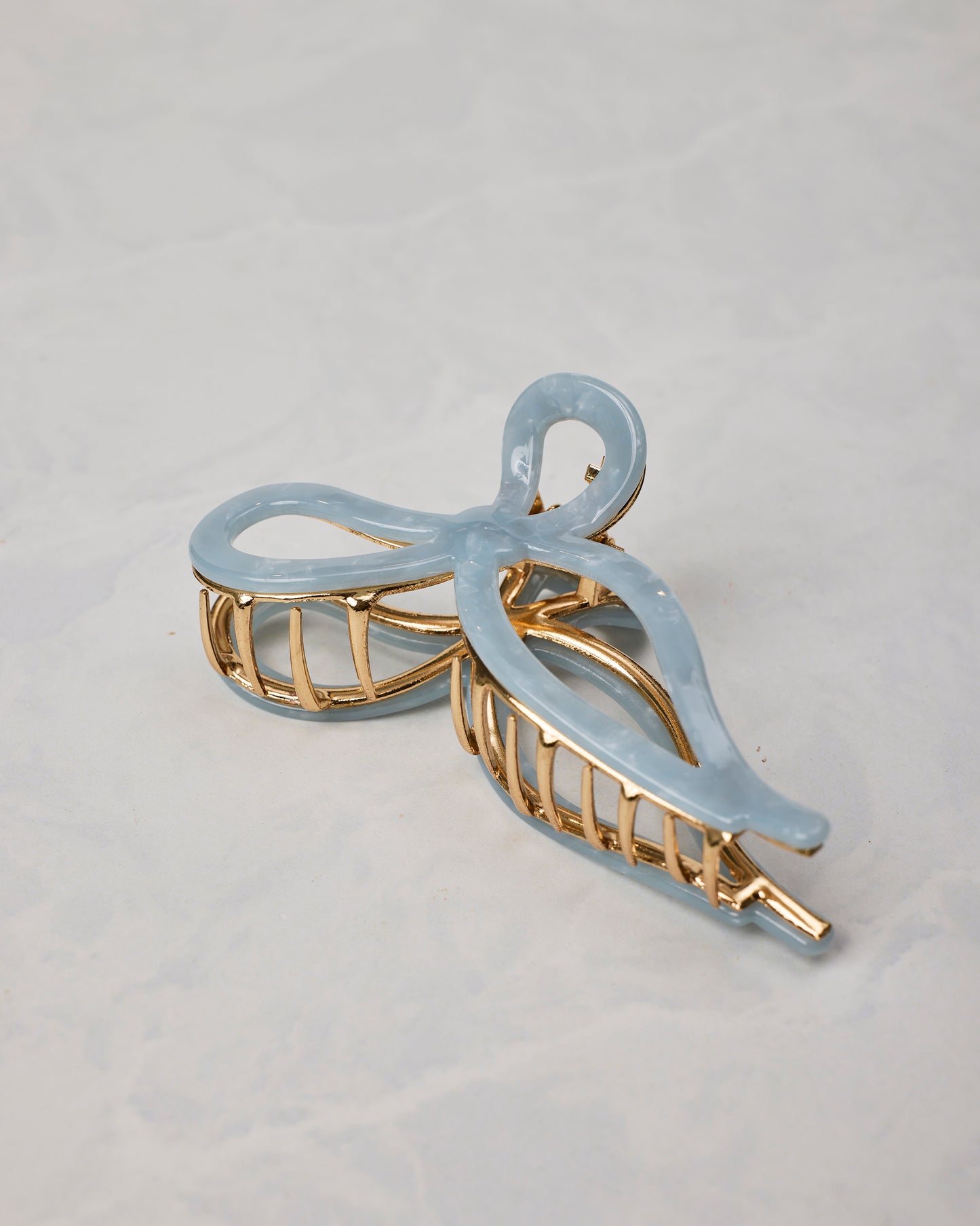 Pale blue ballet bow claw hair clip shown at an angle, with gold-toned teeth and frame.