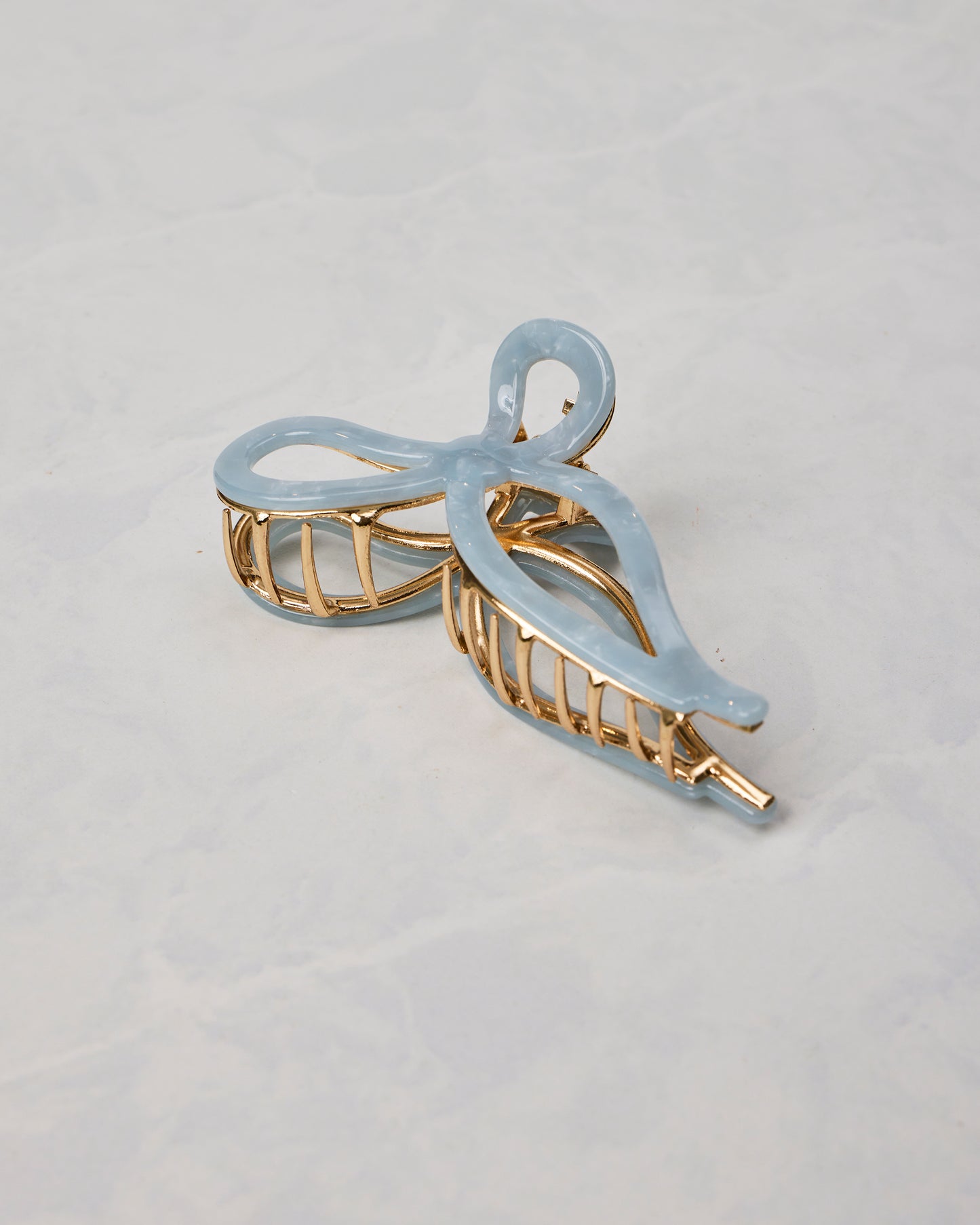 Pale blue ballet bow claw hair clip shown from a different angled view, with gold-toned teeth and frame.