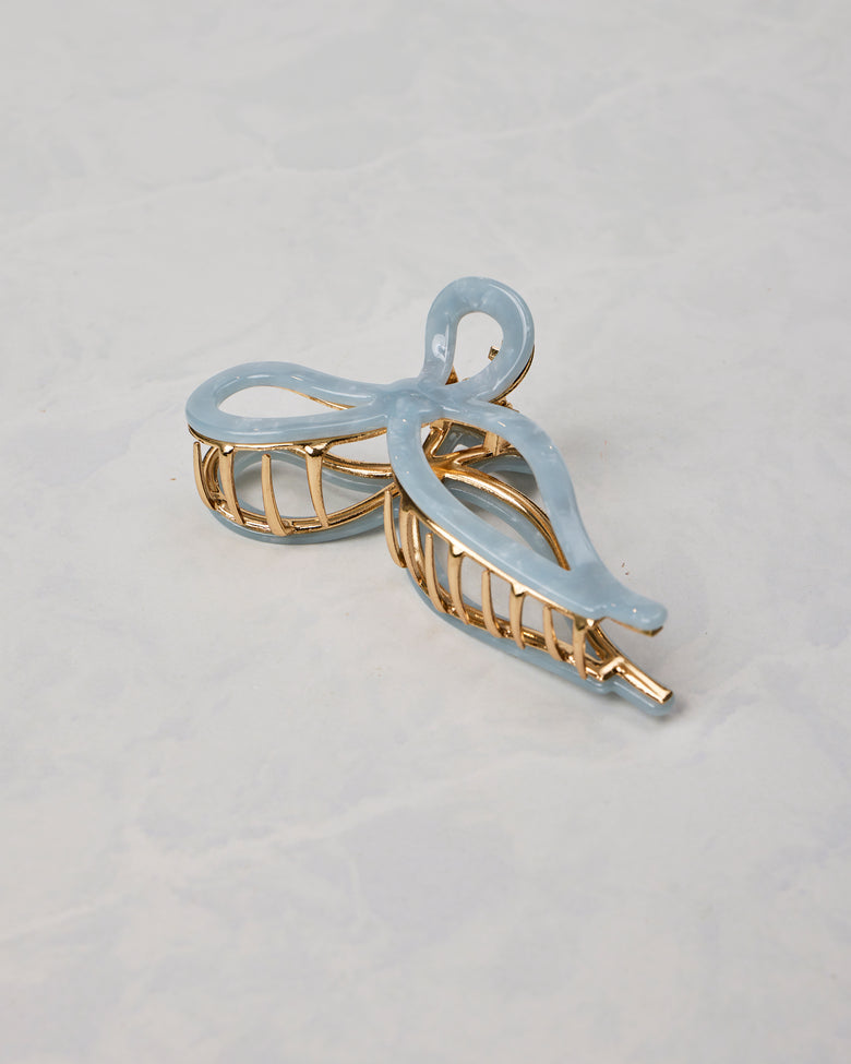 Pale blue ballet bow claw hair clip shown from a different angled view, with gold-toned teeth and frame.