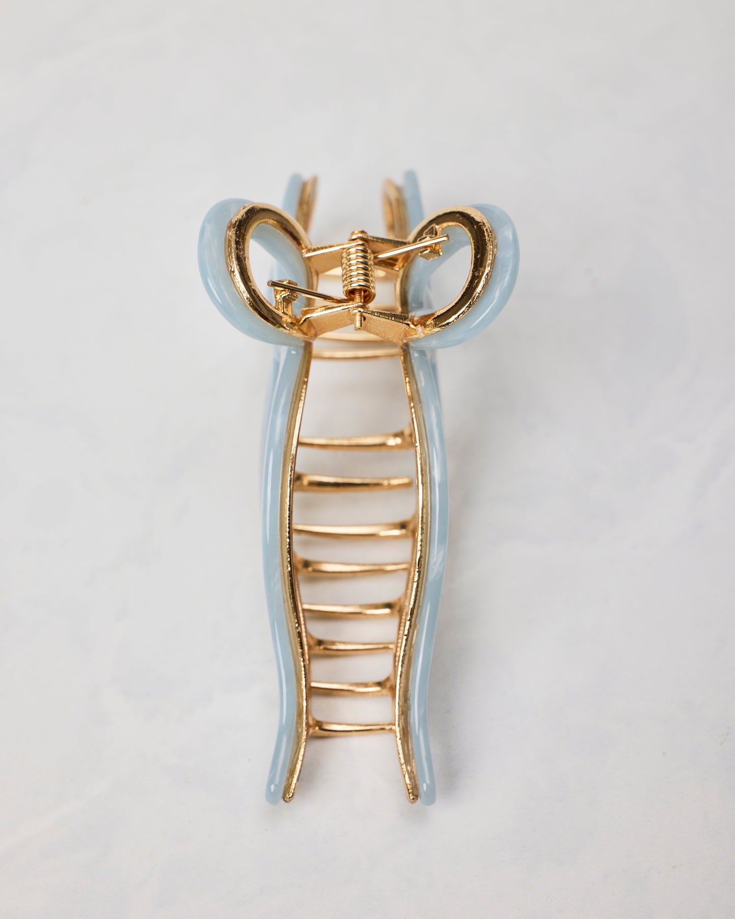 Underside view of a pale blue ballet bow claw hair clip showing its gold-toned spring hinge and teeth.