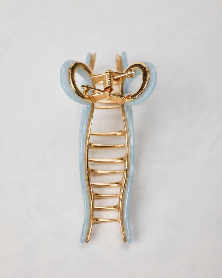Underside view of a pale blue ballet bow claw hair clip showing its gold-toned spring hinge and teeth.